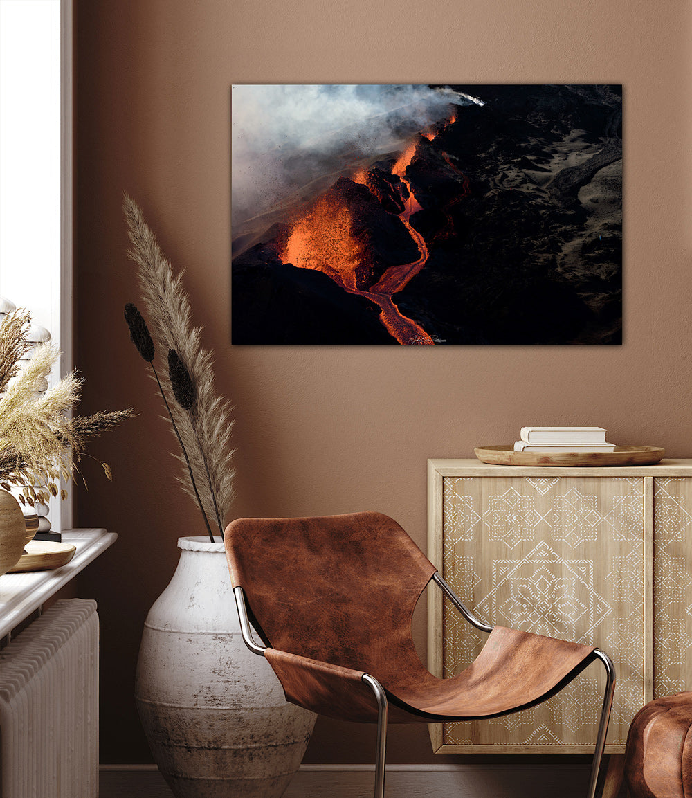 Lava Edge, Piton de la Fournaise. Framed artwork of a volcanic eruption in a room with a brown chair and decorative items.